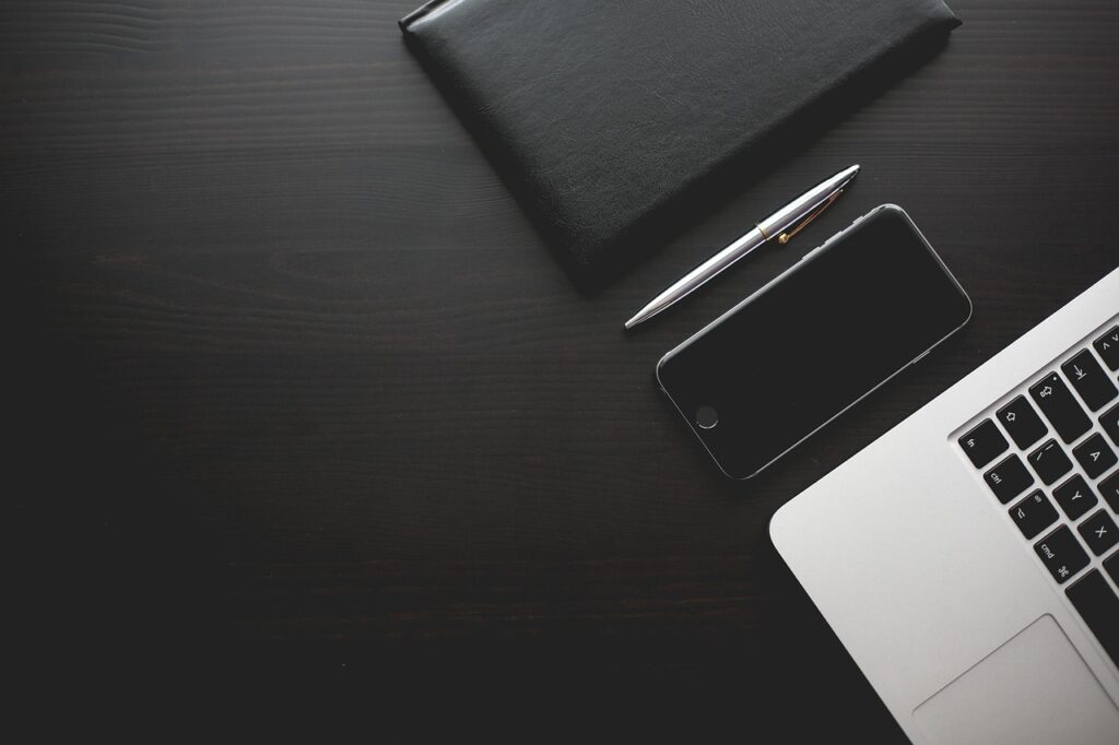 Long-Term Mobile Plans That Bring the Monthly Price Right Down Dark desk with a mobile phone, notebook, pen and laptop