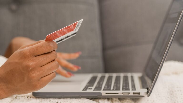 Hand holding a payment card beside an open laptop