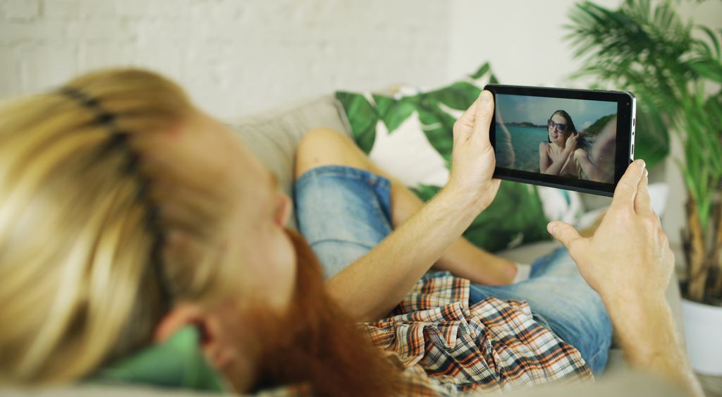 Two people lying on a sofa watching a video together on a phone