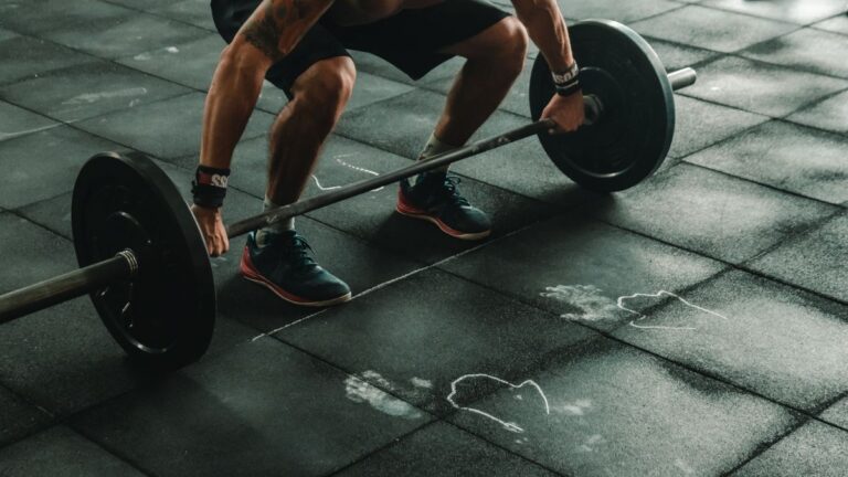 A barbell lift on a gym floor with training shoes in frame
