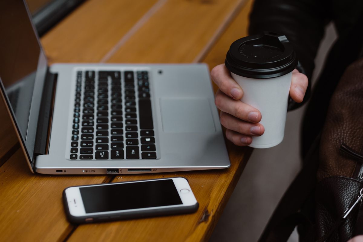 Laptop and smartphone on a wooden table beside a takeaway coffee