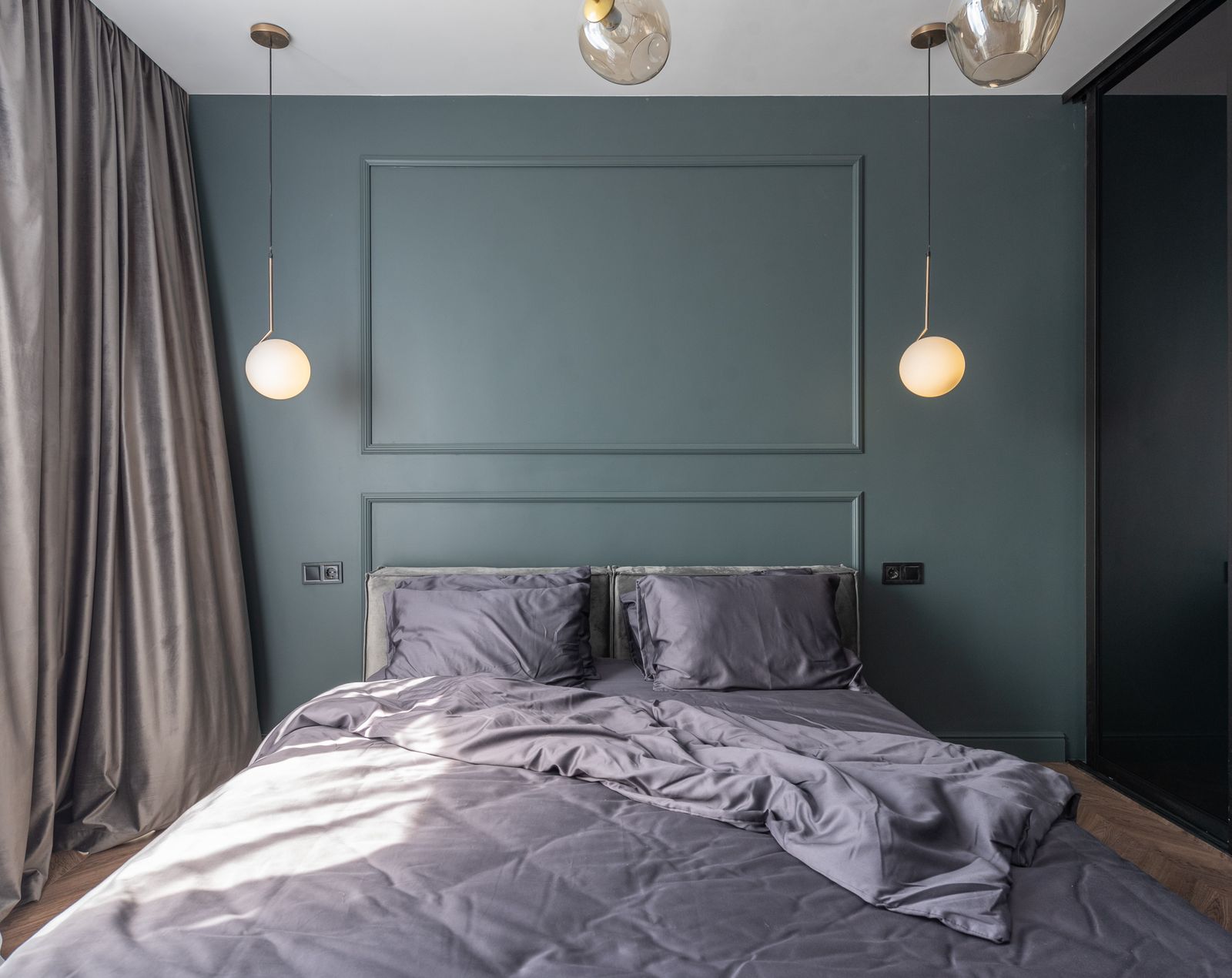 A bed dressed in a soft lilac duvet cover set against a deep green panelled wall