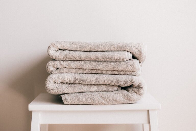 Best Towels to Upgrade a Bathroom Without Redecorating A stack of folded cotton towels on a stool against a white wall