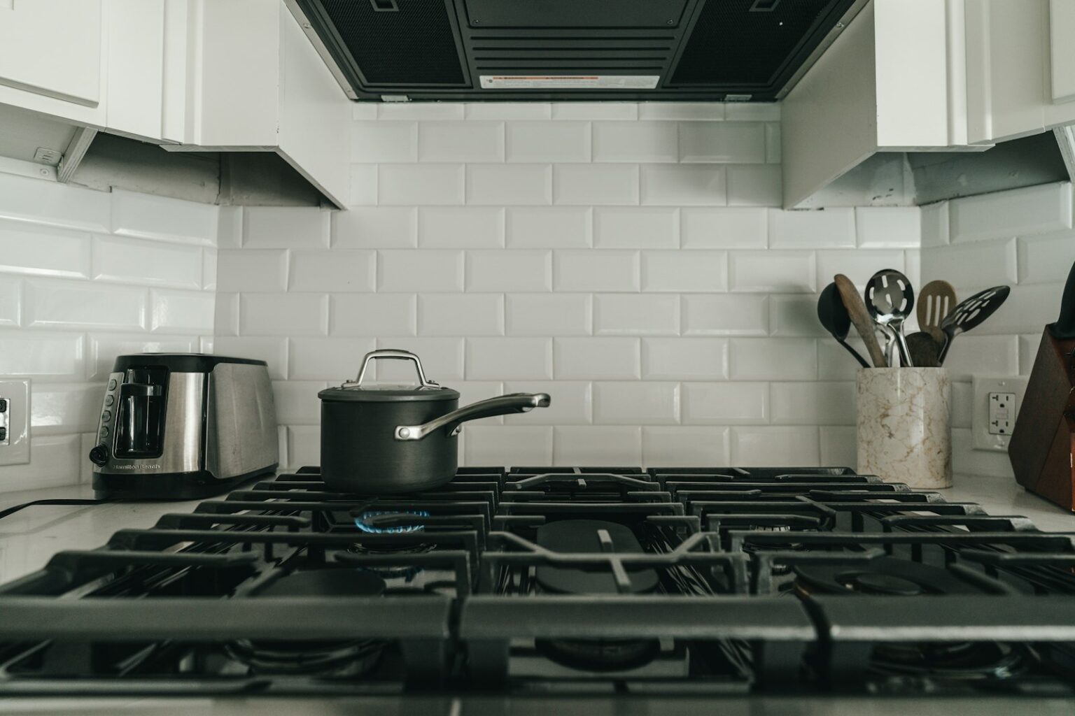 A saucepan on a gas hob in a white-tiled kitchen