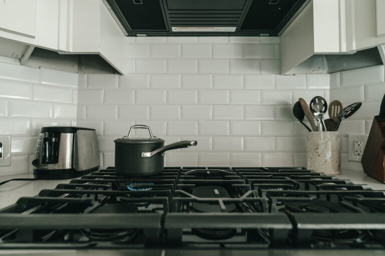A saucepan on a gas hob in a white-tiled kitchen