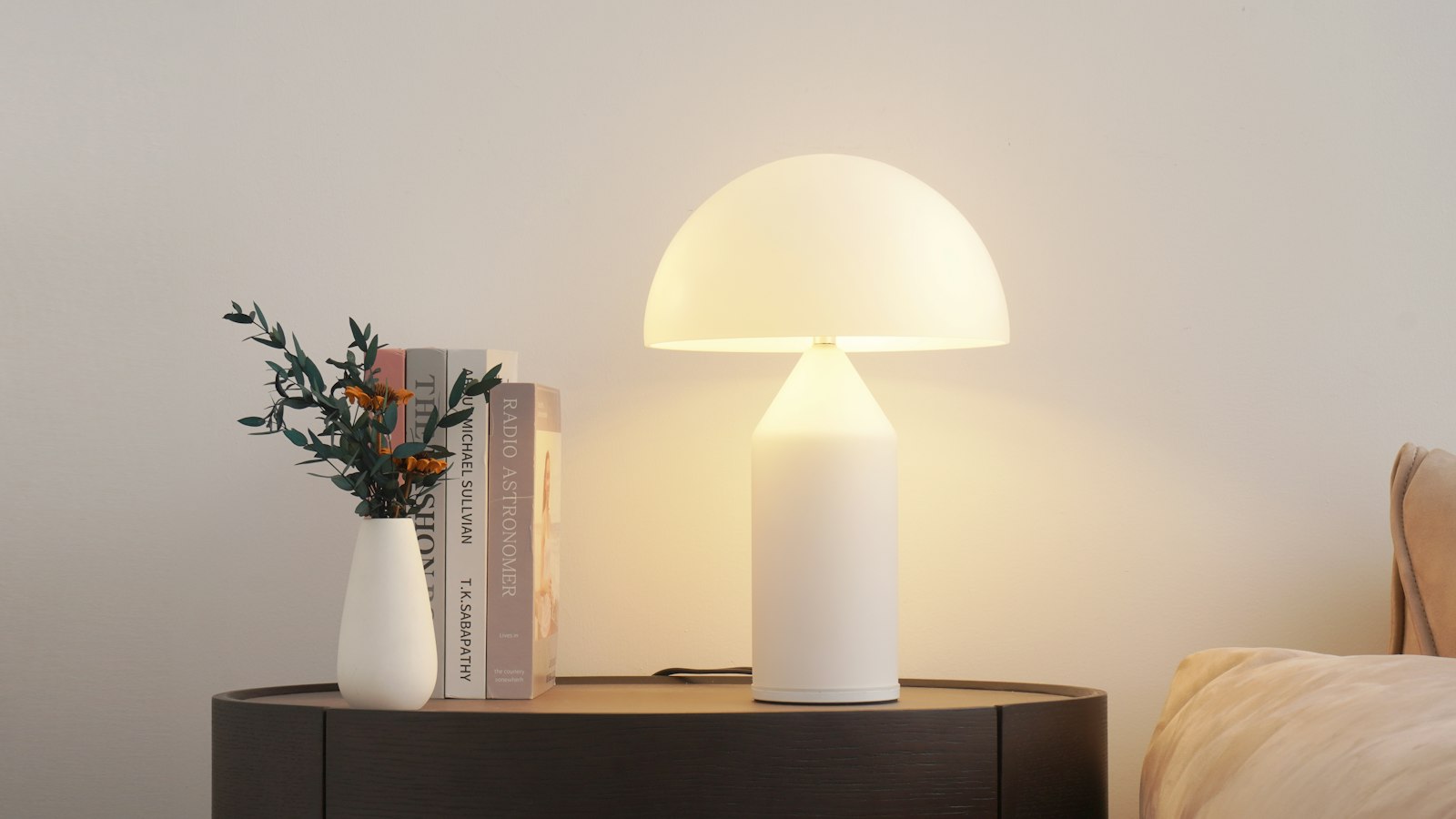 A domed table lamp lit on a console beside books and a vase