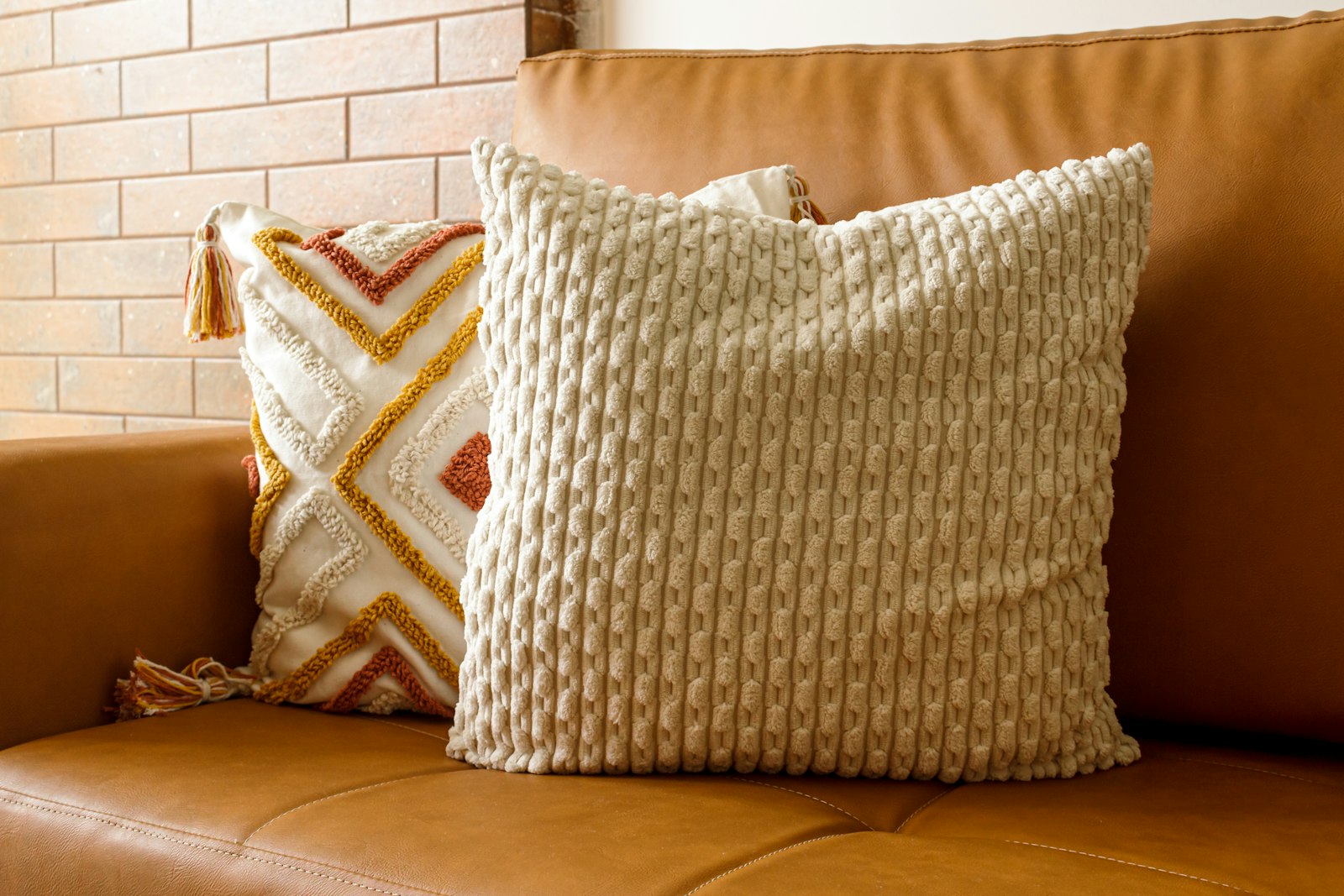 A textured cream cushion on a tan leather sofa