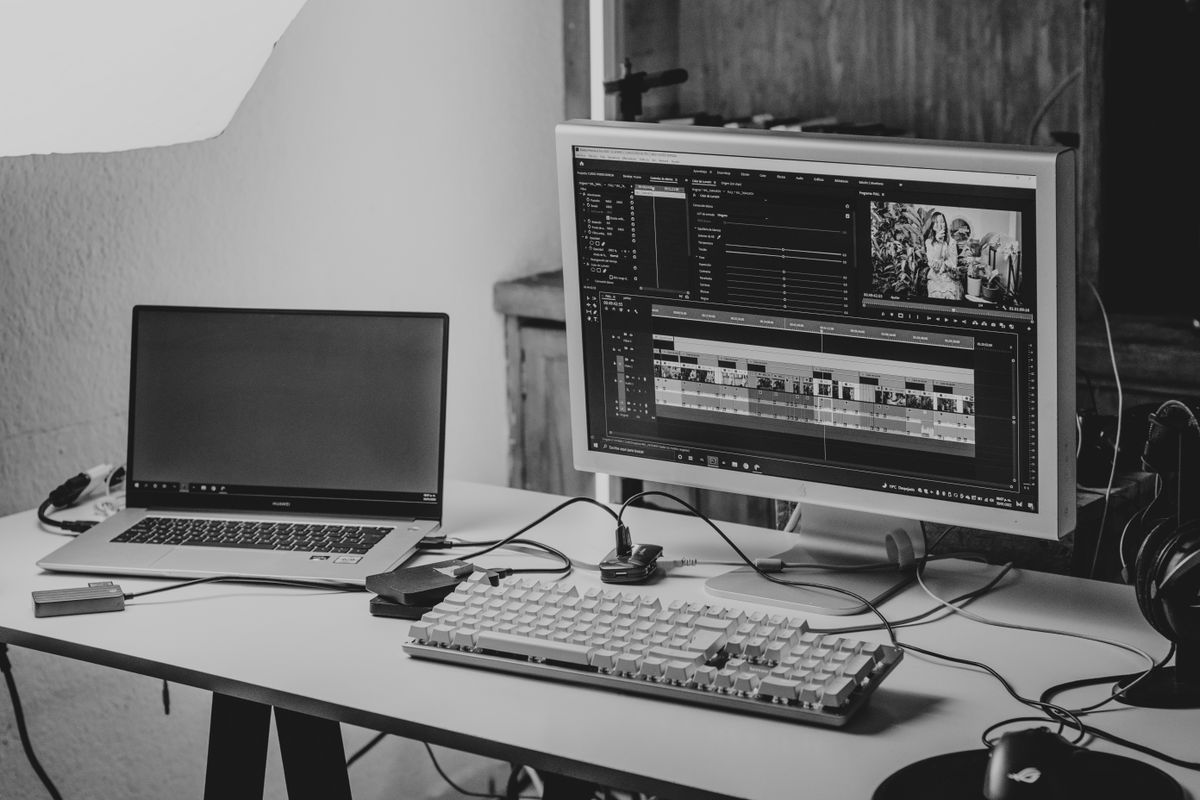 Home video editing desk with a laptop and a monitor showing an edit timeline