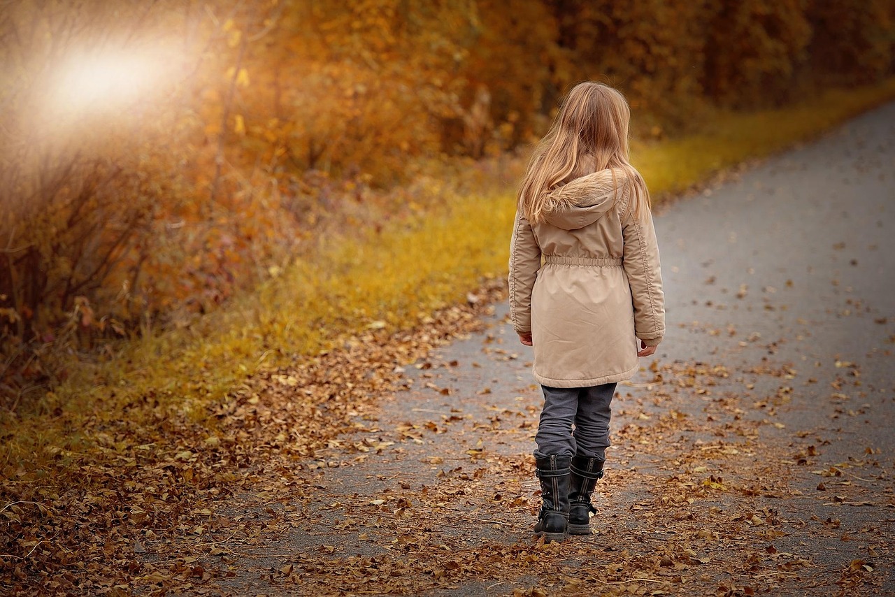 Little girl in ankle boots walking along an autumn path
