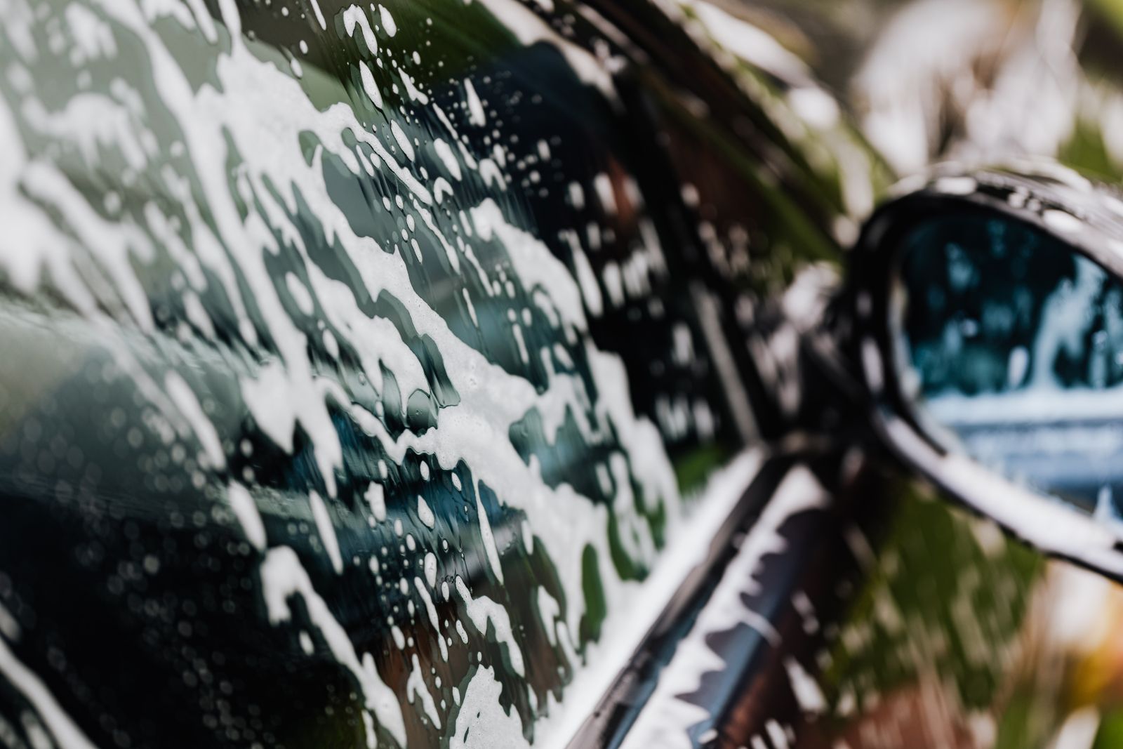 Foam running down the flank of a dark car beside the wing mirror