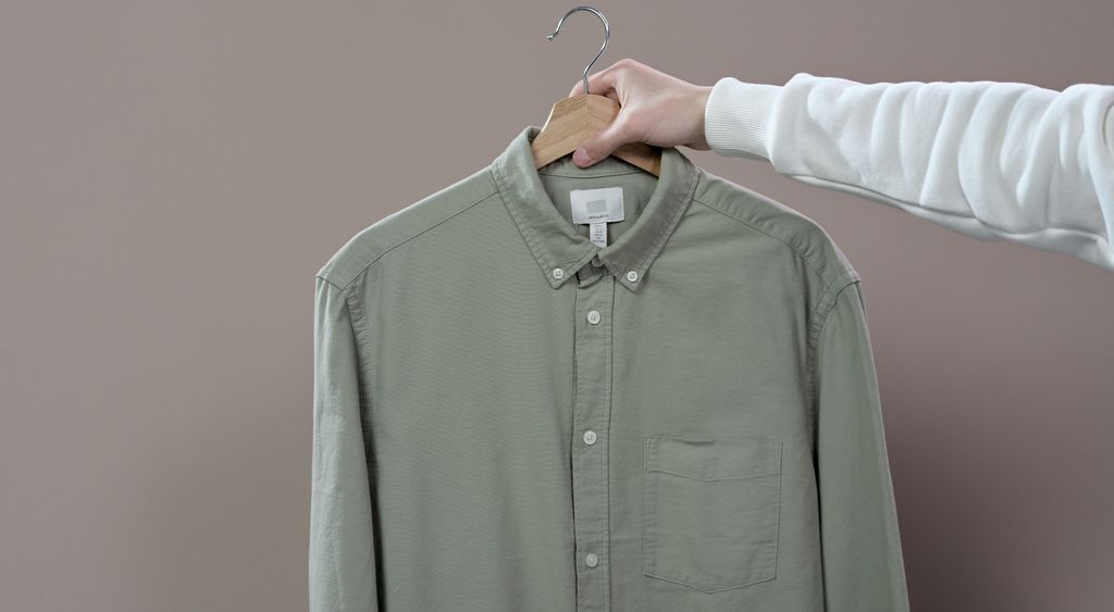 A sage oxford shirt hanging on a rail