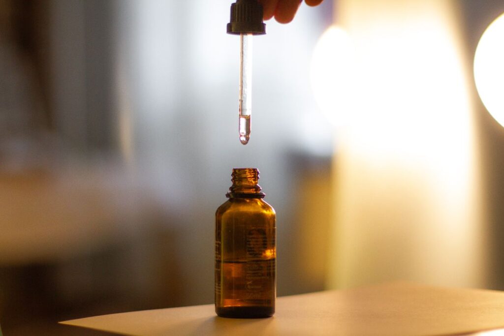 Sérums Visage pour Hydrater et Lisser la Peau Pipette held above an amber glass serum bottle in warm light