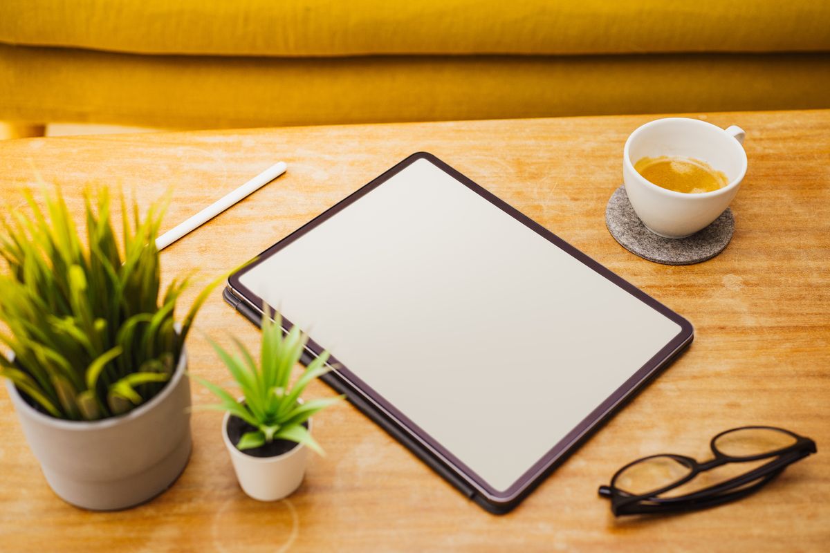 Tablet on a wooden table beside a cup of tea and reading glasses