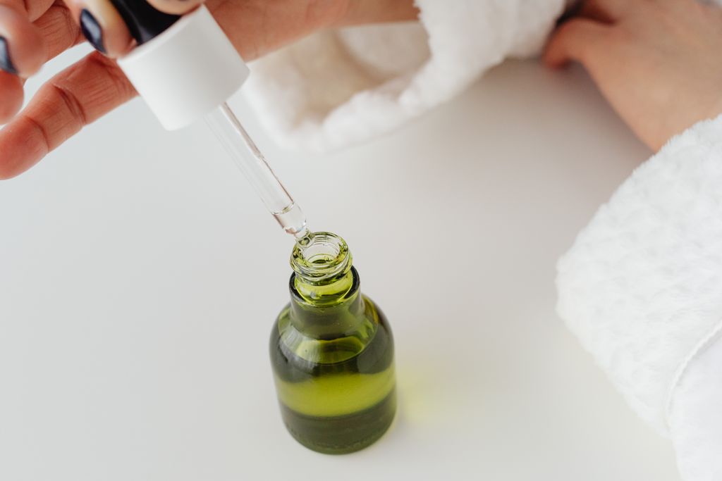 Hand holding a pipette over a green glass serum bottle