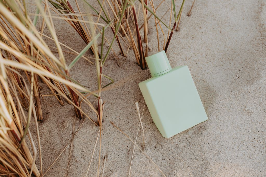 Pale green perfume bottle resting on sand among dune grass