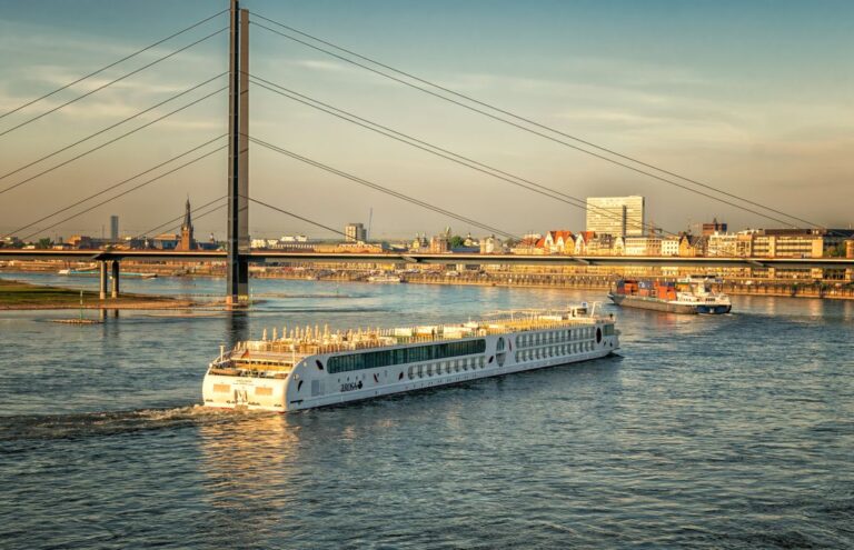 River cruise ship sailing past a city bridge at sunset