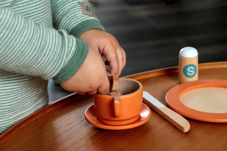 Child playing with a wooden tea set on a tray